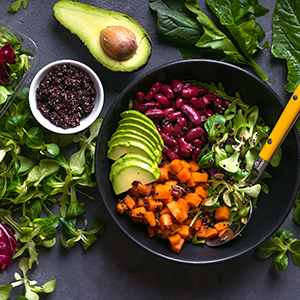 Quinoa salad in bowl with avocado sweet potato beans herbs spinat on concrete rustic background. Quinoa superfood concept. Clean healthy detox eating. Vegan/vegetarian food. Making healthy salad